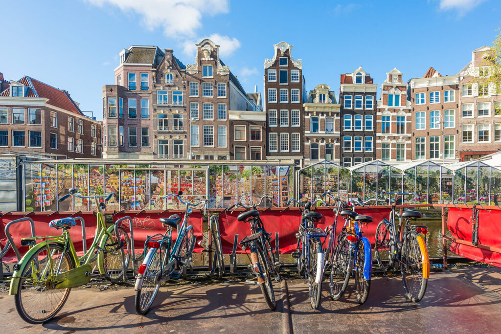Bicicletas aparcadas frente al mercado de flores en Ámsterdam con casas típicas al fondo.